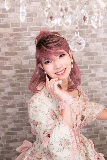 花柄ドレスの女装男子が、シャンデリアの下で頬に手を添え微笑む。上品でロマンティックな一枚。女装サロン「ベルマリ」にて。