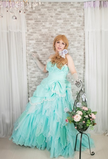 ライトブルーのドレス姿の女装男子が優雅にポーズ。花とリボンが彩る幻想的な空間。女装サロン「ベルマリ」での一枚。