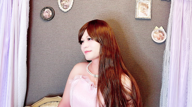女装男子が2着目のピンクドレスに身を包み、ソファーに座り優雅に微笑むワンシーン。憧れの"姫気分"を静かに満喫中です。女装サロン「ベルマリ」では、一人でこっそり女装を楽しみたい人も過ごしやすいプライベートサロンです。
