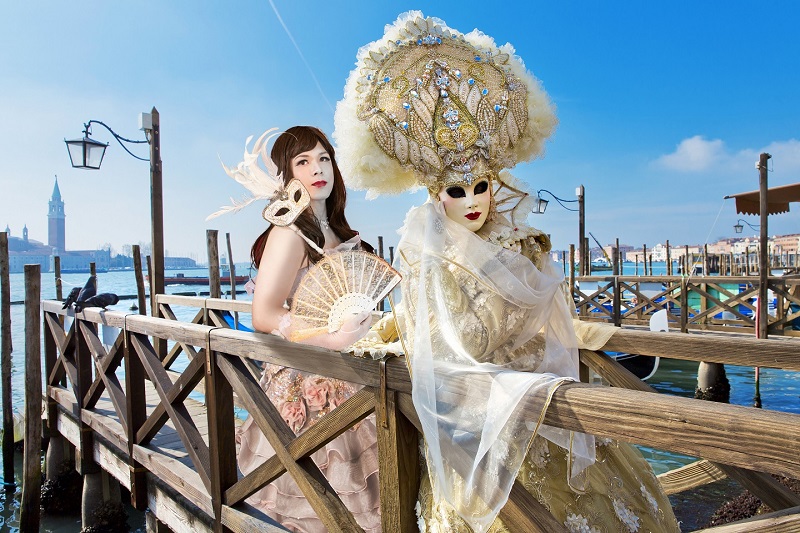 ベネチアの運河沿い、カーニバル衣装の人物と並び立つドレス男子=ジョソンヌ。扇子、仮面など持ち雰囲気もバッチリ。プロのカメラマンが女装サロン「ベルマリ」で本人を撮影し、背景写真にはめ込み完成したメルヘン加工。